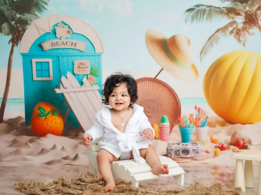 A smiling baby in a white robe on a beach-themed set