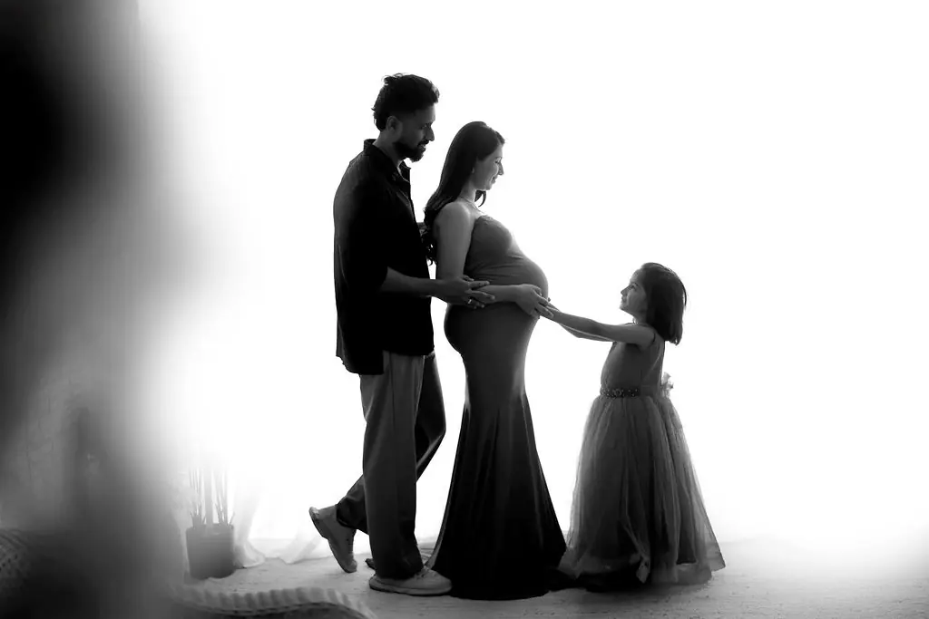 Expectant parents with an older sibling in a tulle dress touching the bump, black and white family maternity portrait at WonderBump Studio, Bengaluru