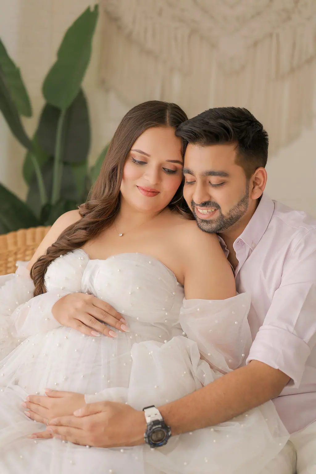 Father embracing an expectant mother from behind in a pearl-dotted white tulle gown, couple maternity portrait at WonderBump Studio, Bengaluru