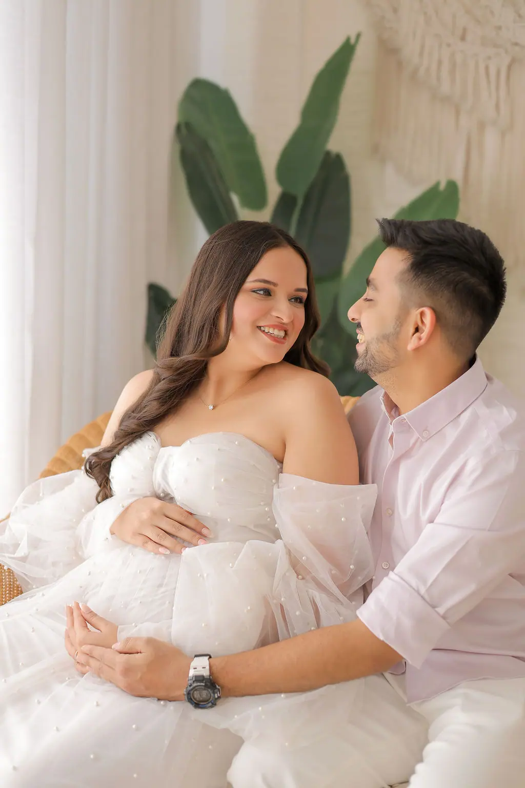 Expectant mother in a pearl-dotted white tulle gown smiling at the father beside her, couple maternity portrait at WonderBump Studio, Bengaluru