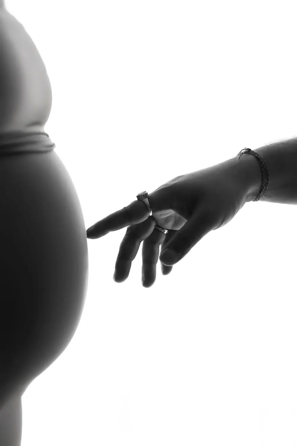 Silhouette of a partner's fingertip gently touching a baby bump against a bright white backdrop, couple maternity portrait at WonderBump Studio, Bengaluru