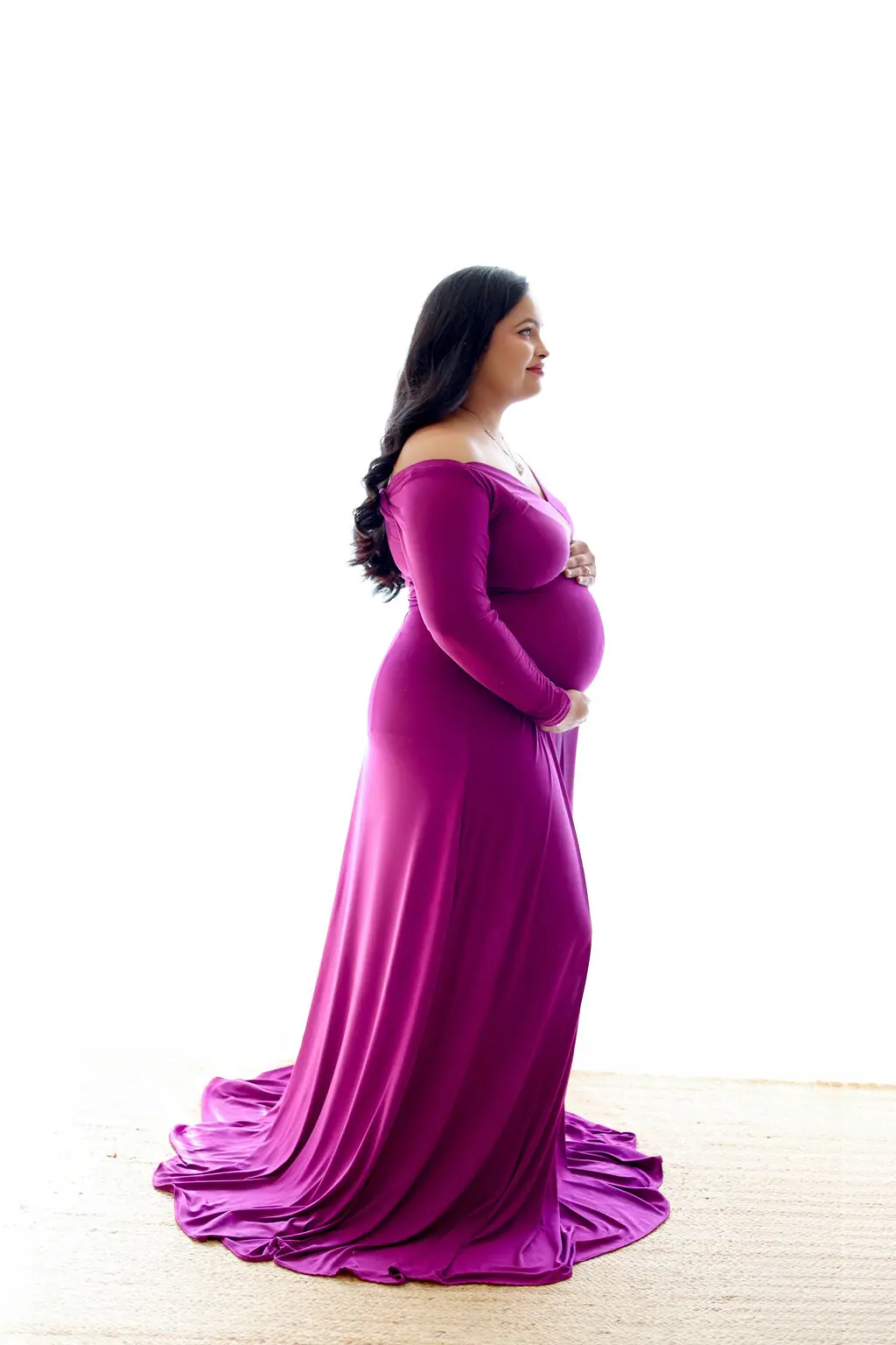 Expectant mother in profile in a magenta off-shoulder gown on a white backdrop, maternity photoshoot at WonderBump Studio, Bengaluru