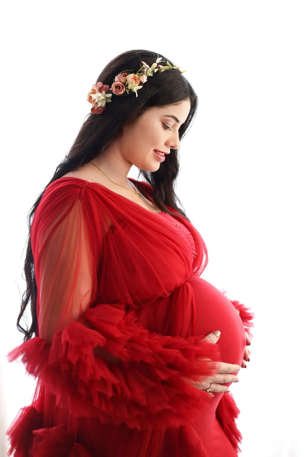 Expectant mother in profile in a red ruffled tulle gown and floral crown, maternity photoshoot at WonderBump Studio, Bengaluru
