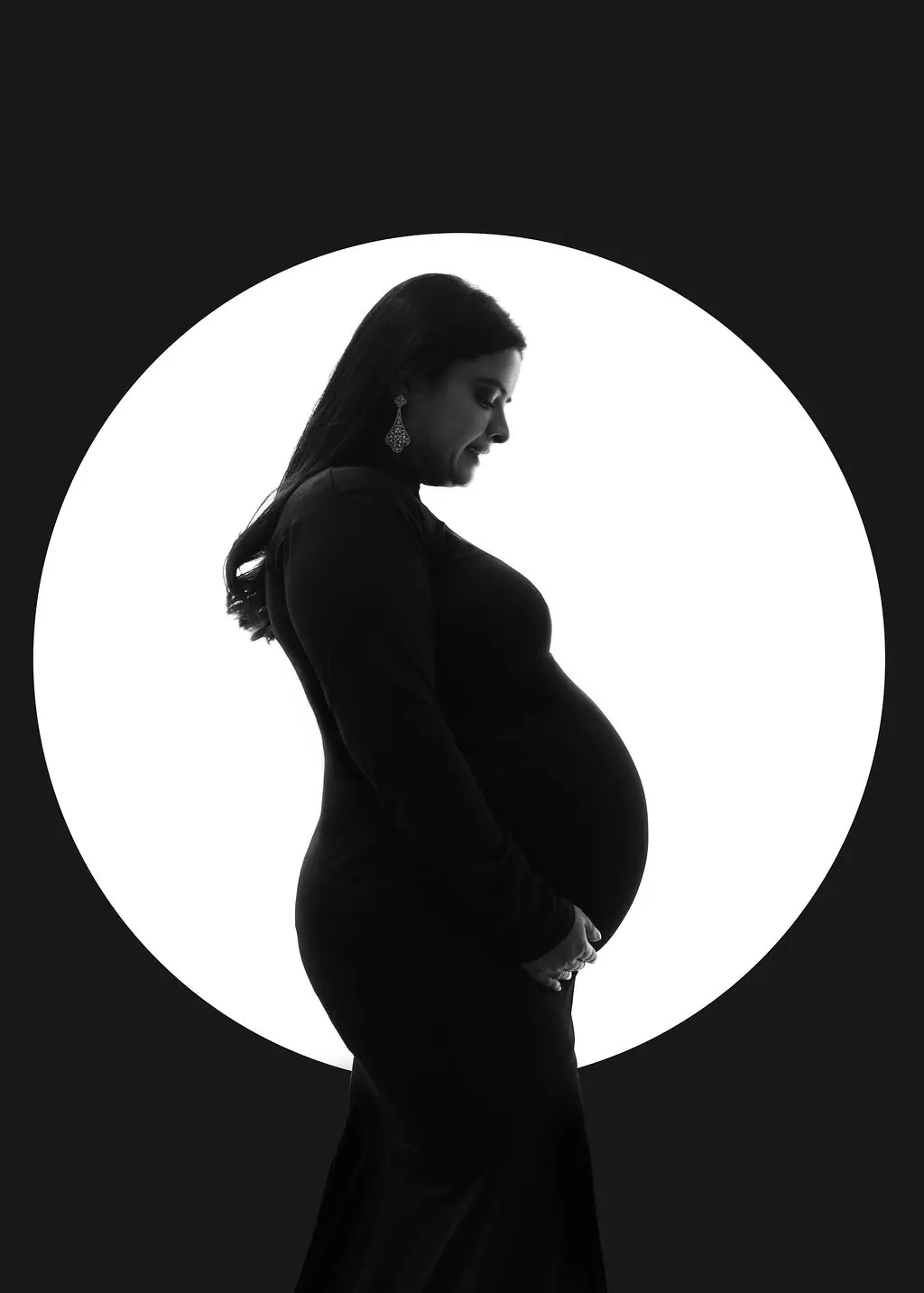 Silhouette of an expectant mother holding her bump against a glowing white circle, maternity photoshoot at WonderBump Studio, Bengaluru