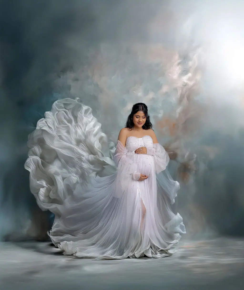 Expectant mother in a white off-shoulder gown with a billowing train, painted cloud backdrop, maternity photoshoot at WonderBump Studio, Bengaluru