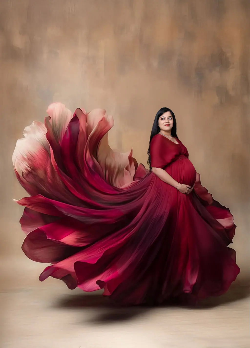 Expectant mother in a wine-red gown whose skirt flows into painted petals, brown backdrop, maternity photoshoot at WonderBump Studio, Bengaluru