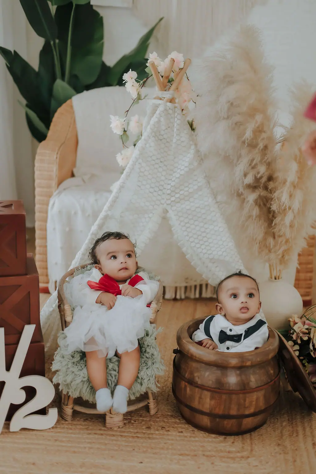 Two babies on a rattan chair and in a wooden pot by a lace teepee, baby milestone photoshoot at WonderBump Studio, Bengaluru