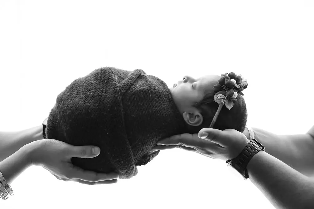Parents' hands cradling a sleeping newborn in a knitted wrap and flower headband, newborn photoshoot at WonderBump Studio, Bengaluru