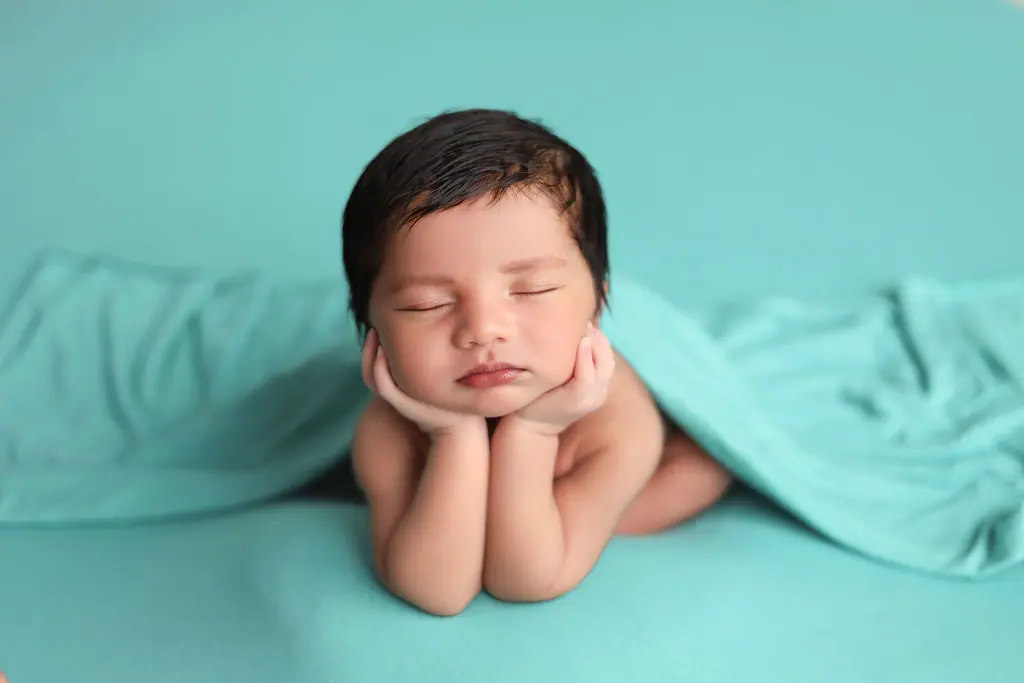 Sleeping newborn in a chin-on-hands pose under a draped aqua wrap on a matching aqua backdrop, newborn photoshoot at WonderBump Studio, Bengaluru