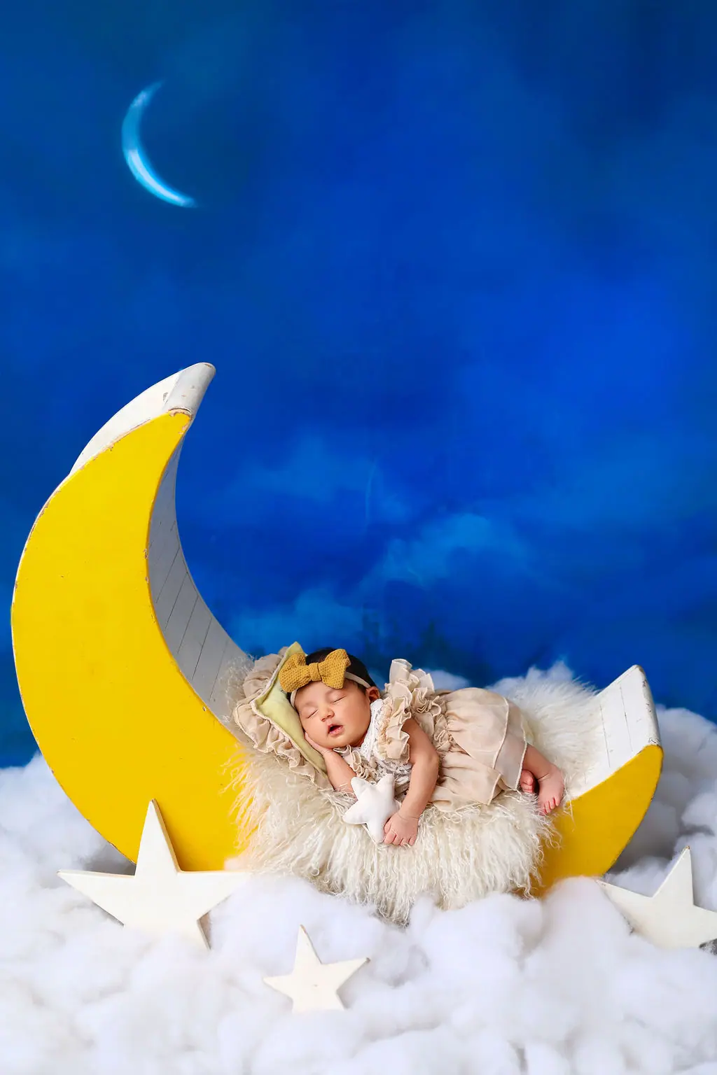 Sleeping newborn on a crescent moon prop with clouds before a painted night sky, newborn photoshoot at WonderBump Studio, Bengaluru