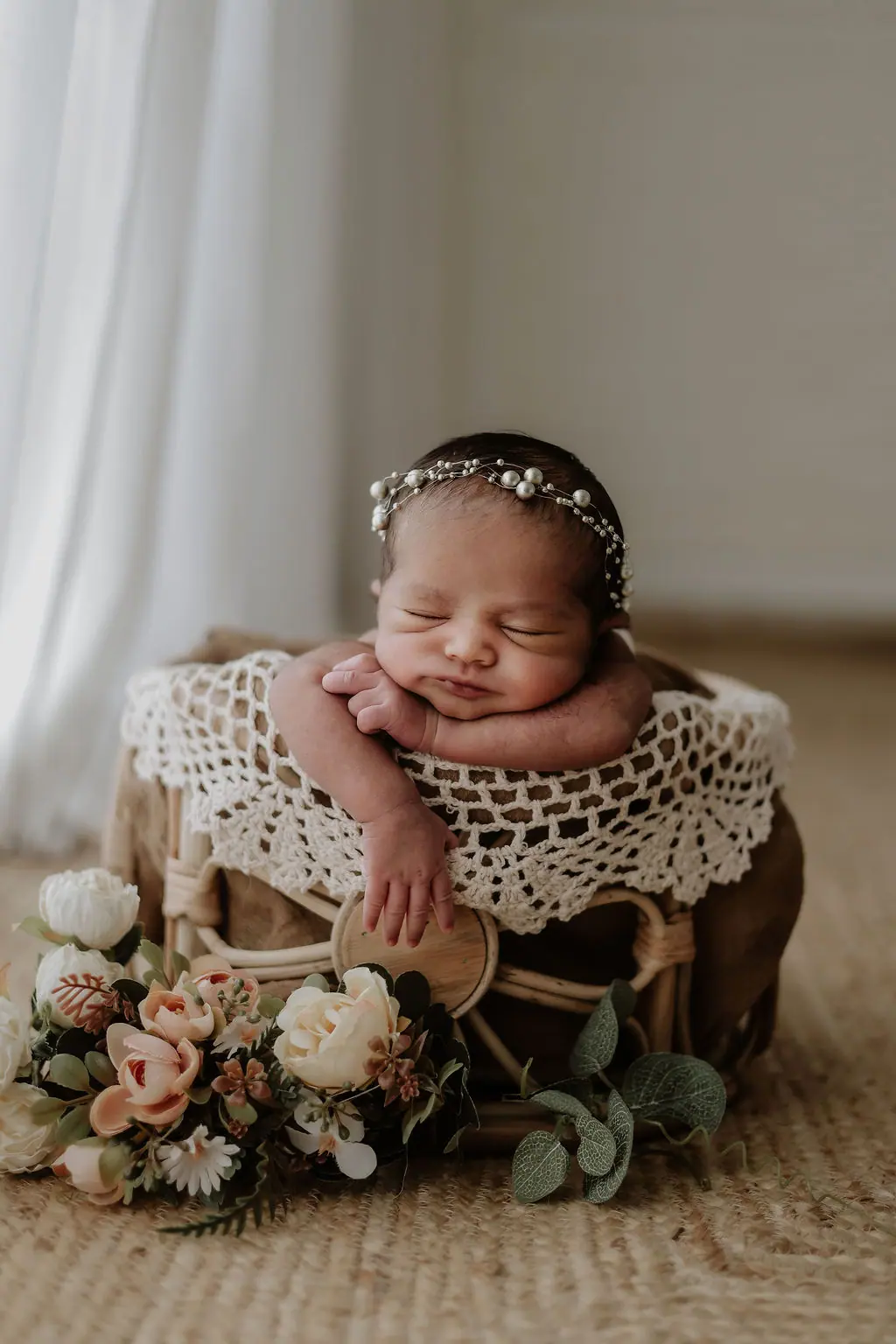 Sleeping newborn in a pearl headband on a lace-draped rattan basket with roses, newborn photoshoot at WonderBump Studio, Bengaluru