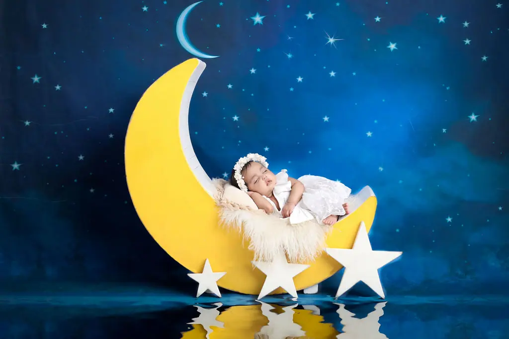 Baby asleep on a fur-lined crescent moon prop, painted starry night backdrop, baby photoshoot at WonderBump Studio, Bengaluru