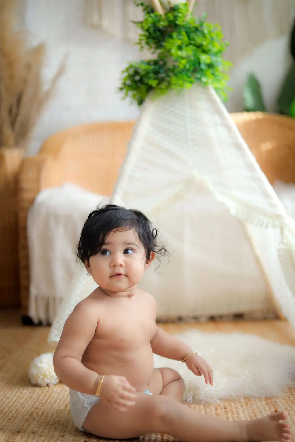 Baby sitting on a fur rug in a nappy and gold bangles before a lace teepee, toddler photoshoot at WonderBump Studio, Bengaluru