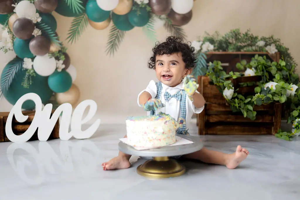 Laughing toddler in a bow tie with a sprinkle cake, balloon arch and One sign, toddler photoshoot at WonderBump Studio, Bengaluru