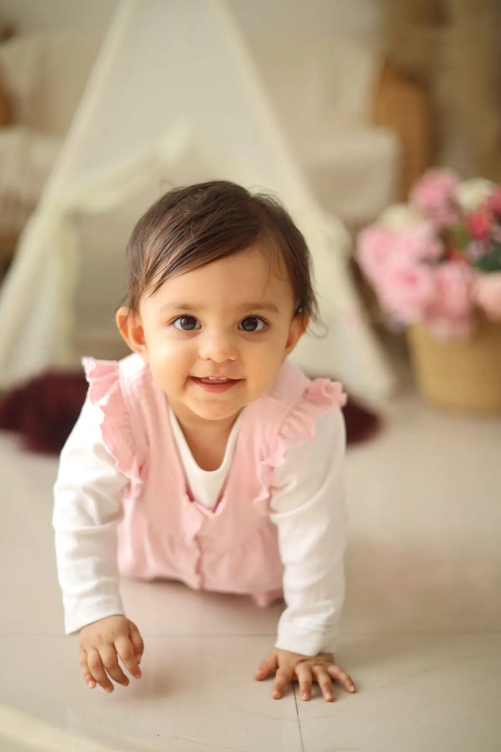 Smiling baby crawling towards the camera in a pink ruffled romper by a teepee, toddler photoshoot at WonderBump Studio, Bengaluru